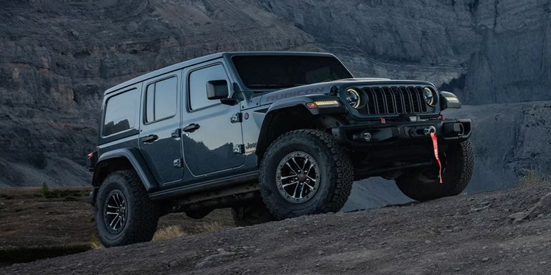 A dark slate gray Jeep Wrangler Rubicon four-door driving up a steep, rocky mountain slope.